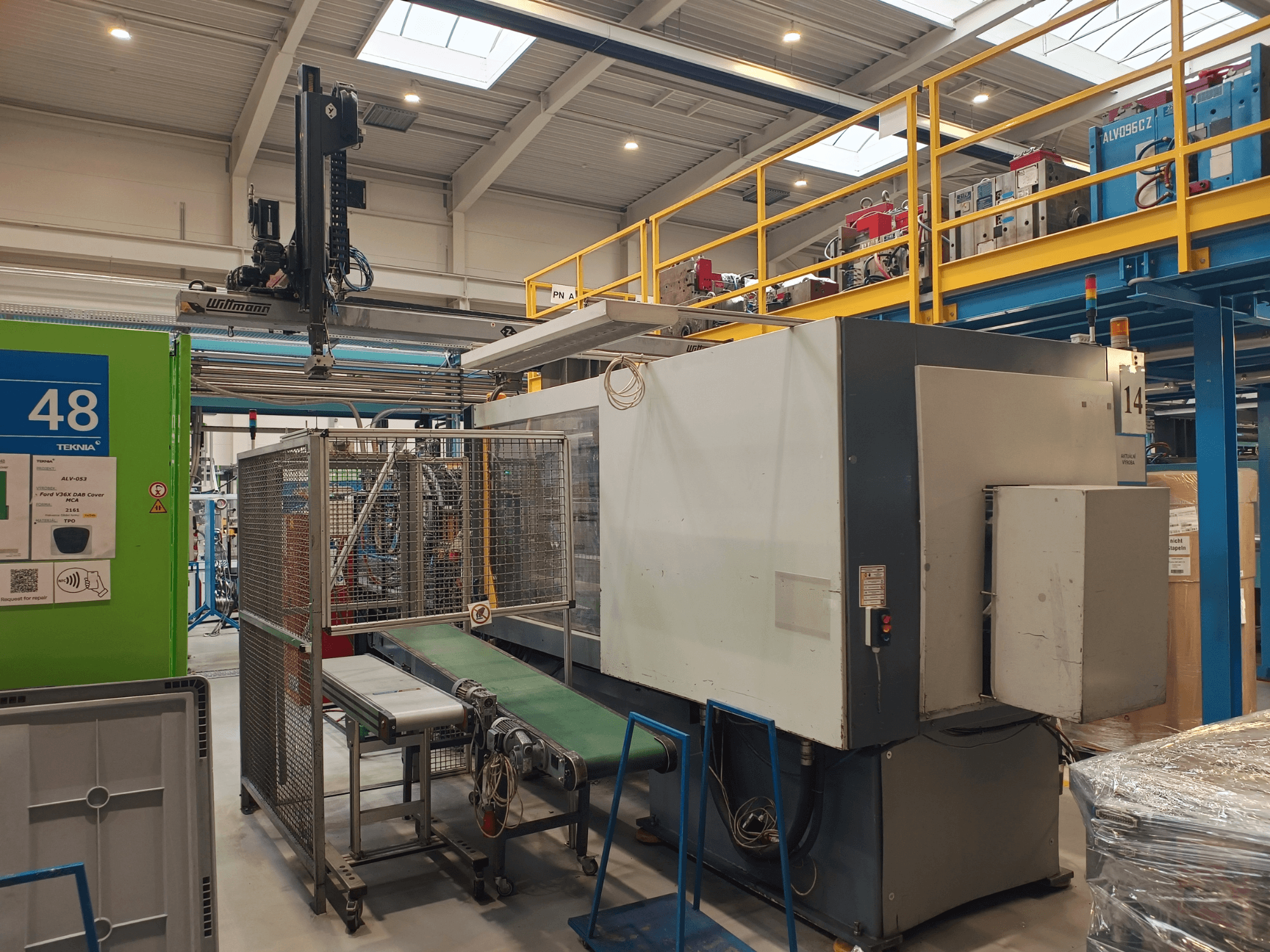 Ipari automatizálási berendezés zöld szállítószalaggal, "48" felirattal és daruval; a gép oldalnézetben a gyárban.