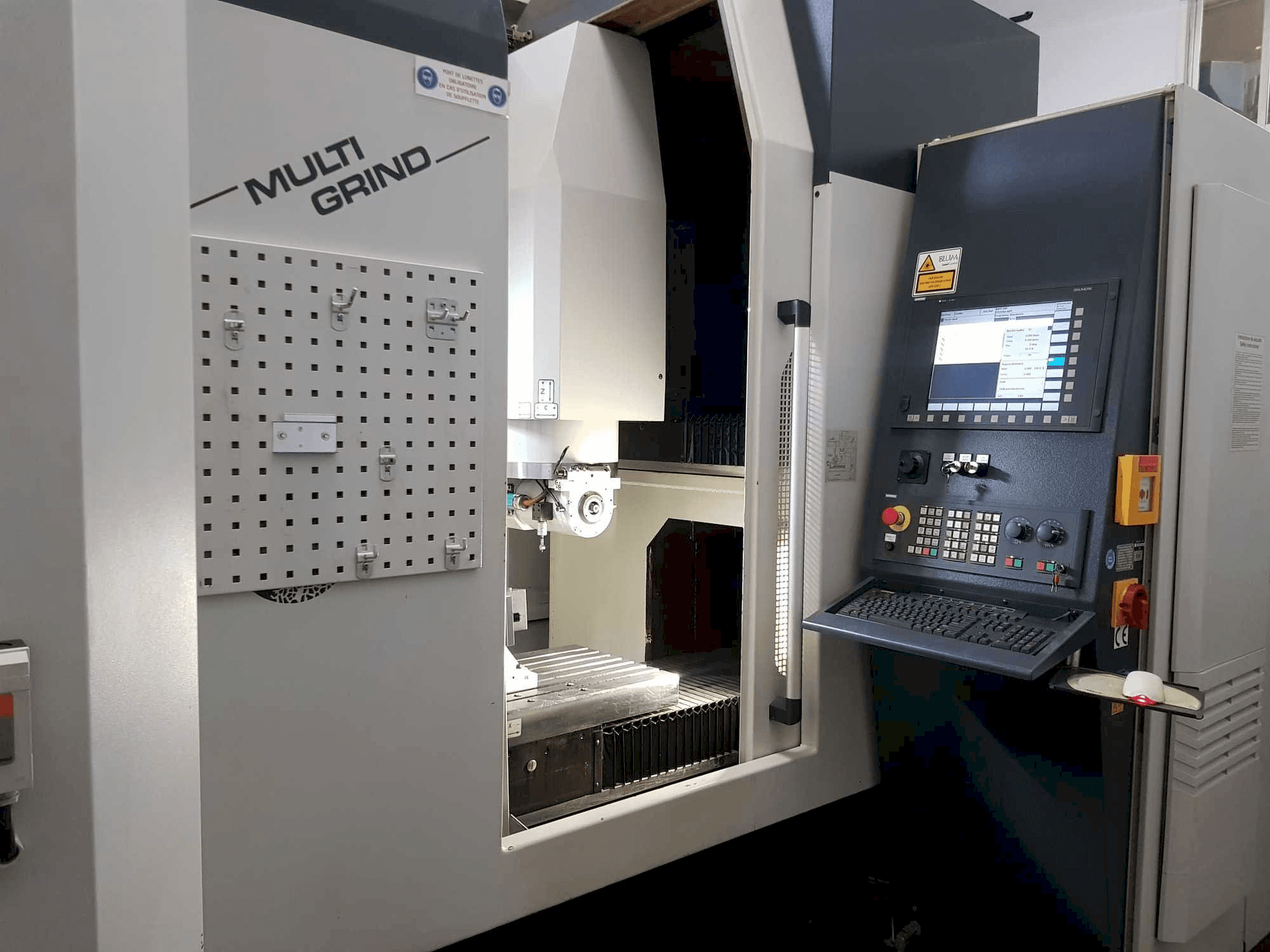 Multi Grind CNC-gép elölnézetben, vezérlőpanellel, tárolószegéllyel és nyitott munkaterülettel.